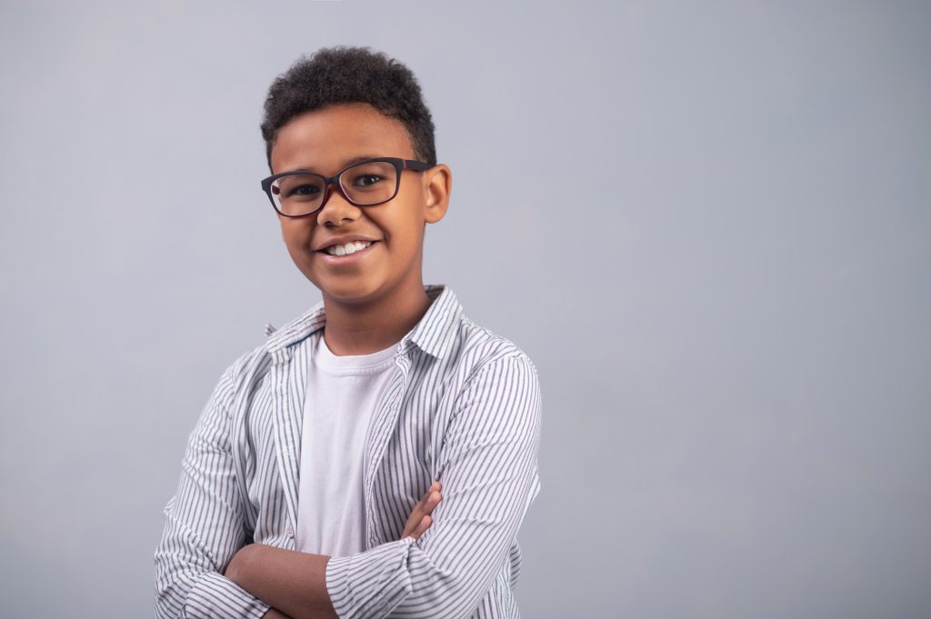African American child smiling in a waist up headshot with his arms folded